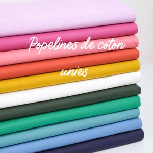 Peut inclure: Une pile de tissus en coton de différentes couleurs unies, dont rose, rouge, jaune, vert et bleu. Le texte "Popelines de coton unies" est écrit sur le tissu.