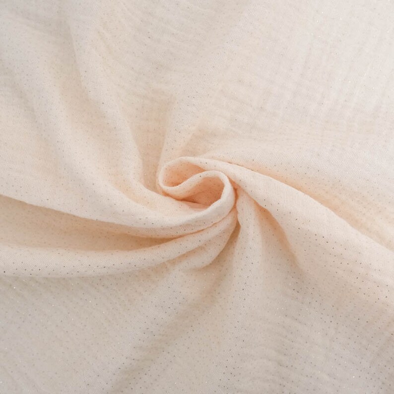 May include: A close-up of a soft, peach-coloured fabric with a subtle shimmer. The fabric has a slightly textured surface and is draped in a loose, flowing manner.