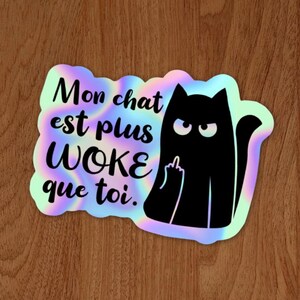 May include: A sticker featuring the French text "Mon chat est plus WOKE que toi." and a black cat silhouette. The cat is giving the middle finger. The background has a holographic, iridescent effect.