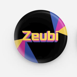 May include: A round, black button with the word "Zeubi" in yellow, outlined in blue and pink. The button has a retro design with yellow, pink, and blue geometric shapes radiating from the center.