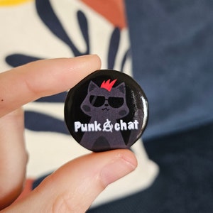 May include: A black button with the text "Punk & chat". The button features a cartoon cat wearing sunglasses and a red mohawk. The cat is gray, and the text is white.