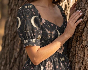 May include: A black dress with a sweetheart neckline and puff sleeves, featuring a repeating pattern of white crescent moons, pink flowers, and butterflies. The fabric has a dark base with botanical illustrations and celestial motifs throughout.