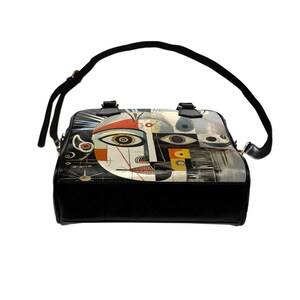 May include: Black and white shoulder bag with a unique abstract face design. The bag features a black base, a long black strap, and two short handles. The face design includes orange, red, and yellow accents, with multiple eyes and geometric shapes.