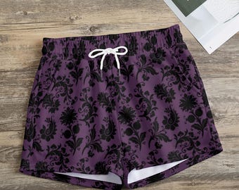 Pode incluir: Calções roxos com um padrão floral preto e cordão branco. Os calções têm bolsos e uma cintura elástica confortável. São feitos de um material macio e leve.