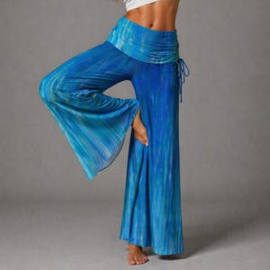 Könnte beinhalten: Blaue Palazzo-Hose mit Aquarell-Effekt. Die Hose mit weitem Bein hat einen hohen, gerafften Bund und einen Kordelzug. Der Stoff hat ein fließendes, leichtes Aussehen mit vertikalen Streifen in Blau und Türkis.