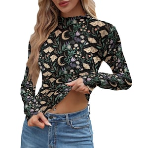 Könnte beinhalten: Schwarzes Langarmshirt mit floralem und Mottenmuster. Das Design umfasst Halbmonde, Blumen und Motten in Creme-, Grün- und Lilatönen. Das Shirt hat einen hohen Ausschnitt.