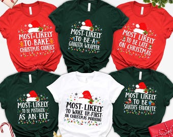 May include: A collection of Christmas-themed t-shirts in red, green, and white. Each shirt features a Santa hat and text like "Most Likely to Bake Christmas Cookies" or "Most Likely to Be Santa's Favorite."