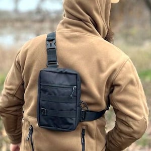May include: A person wearing a brown fleece jacket with a black crossbody bag. The bag has a zippered closure and a strap that goes over the shoulder.