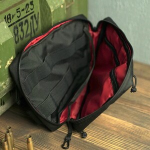 May include: Black zippered pouch with red lining and multiple compartments. The pouch is open and the interior is visible.