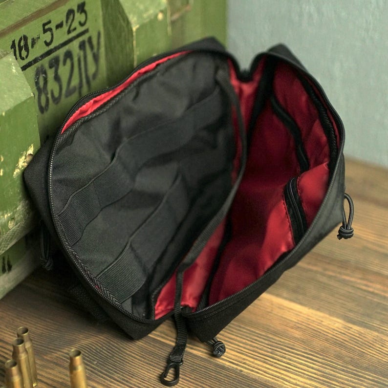 May include: Black zippered pouch with red lining and multiple compartments. The pouch is open and the interior is visible.