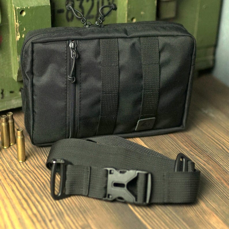 May include: A black tactical bag with a zipper closure and an adjustable shoulder strap. The bag has multiple compartments and is made of durable nylon.