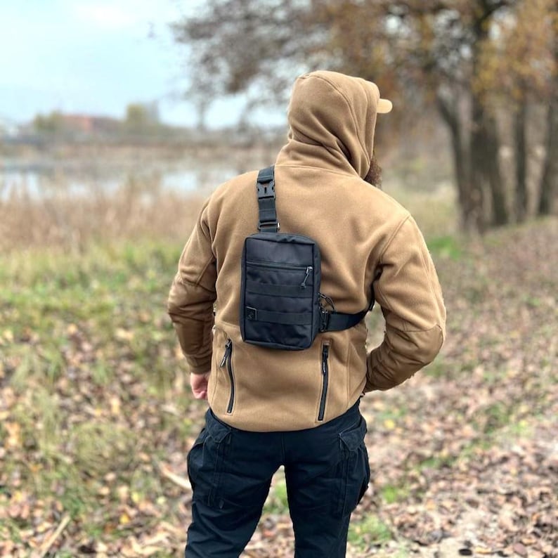 May include: A person wearing a brown fleece jacket with a black crossbody bag. The bag has a zippered closure and a strap that goes over the shoulder.