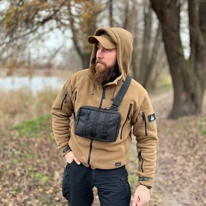 May include: A person wearing a brown fleece jacket with a black crossbody bag. The bag has a zippered closure and a strap that goes over the shoulder.
