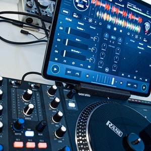 Op de afbeelding: Een zwarte DJ-mixer met knoppen en draaiknoppen, een zwarte draaitafel met een zilveren RANE-logo en een tablet met een DJ-software-interface met een golfvorm en bedieningselementen.