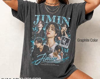 Könnte beinhalten: Ein graphitfarbenes Kurzarm-T-Shirt mit einem Grafikdruck des Künstlers Jimin. Das Design zeigt mehrere Porträts, den Schriftzug JIMIN in einer blauen Glitzerschrift sowie kleinere Textelemente wie You're my blue, Like Crazy und Park Jimin.