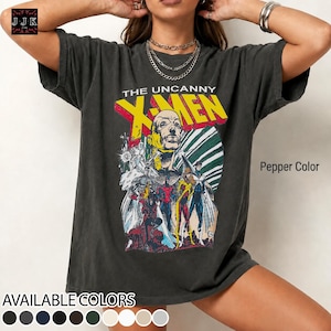 May include: A pepper-colored short-sleeve t-shirt featuring a graphic print of The Uncanny X-Men with Professor X at the top and various characters below. The text reads THE UNCANNY X-MEN in bold yellow letters against a dark background.