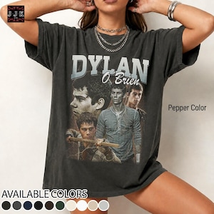 Può includere: T-shirt color pepe con grafica di Dylan O'Brien. Il design include più immagini dell'attore e la scritta "DYLAN O'BRIEN". La maglietta ha anche un elenco dei colori disponibili.