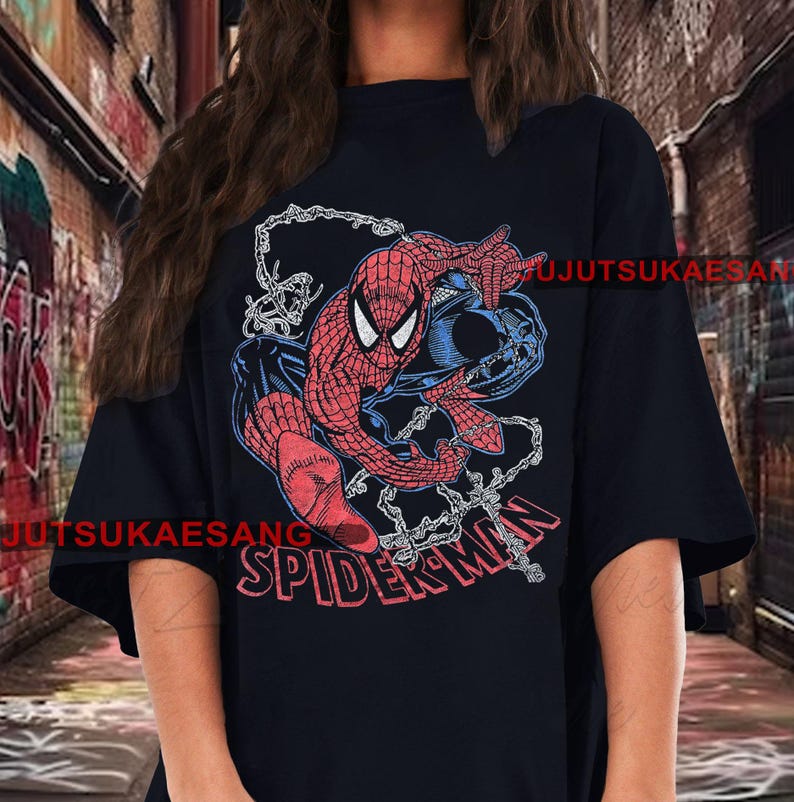 May include: Black t-shirt featuring a graphic of Spider-Man in red and blue, with the word "SPIDER-MAN" in red. The design includes a web and a blue background element. The shirt is a casual wear item.