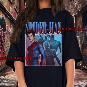 May include: Black t-shirt featuring a graphic of Spider-Man, with the text "SPIDER-MAN" in blue and purple, and "Andrew Garfield" in white script. The graphic includes images of the actor Andrew Garfield in the Spider-Man suit.