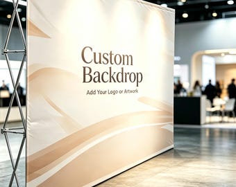 May include: A large, custom backdrop with a cream-colored background and flowing, light brown design elements. The text "Custom Backdrop" is displayed in a dark brown font, with the tagline "Add Your Logo or Artwork" below. The backdrop is supported by a silver metal frame.