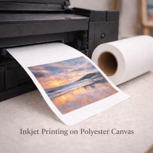 May include: A black inkjet printer printing a landscape image on white polyester canvas. A roll of white canvas sits beside the printer. The printed image shows a sunset over the ocean. Text on the image reads "Inkjet Printing on Polyester Canvas."