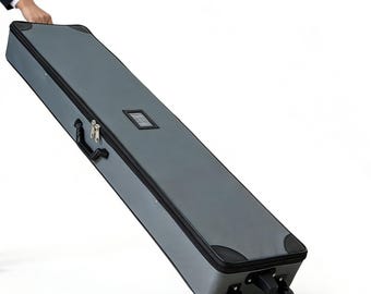 May include: A gray, rectangular rolling case with a black zipper, handle, and corner protectors. The case has a small, rectangular clear window and is being pulled by a person. The case has four wheels.