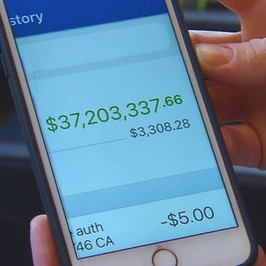 Könnte beinhalten: Smartphone-Bildschirm mit Finanztransaktionsverlauf. Der Bildschirm zeigt einen großen Kontostand von 34.200.000,00 € in grüner Schrift, mit anderen Transaktionen und Beträgen. Das Telefon wird in einer Hand gehalten.