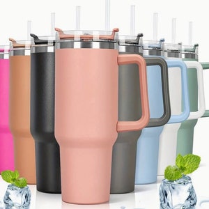 Op de afbeelding: Set van zeven reistassen van roestvrij staal met handvatten en deksels. De bekers zijn in verschillende kleuren, waaronder roze, bruin, zwart, grijs, blauw, wit en groen. Elke beker heeft een rietje.