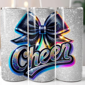 May include: A silver glitter tumbler featuring a large black bow with blue and silver accents. The word "Cheer" is written in a colorful, outlined font. The tumbler has a straw and is designed for cold beverages.