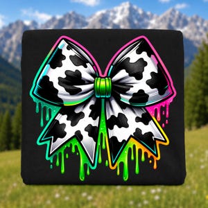 May include: A black fabric square featuring a large, central bow graphic with a black and white cow print pattern. The bow is outlined in vibrant neon pink, green, and orange, with paint-like drips extending downward from the edges.