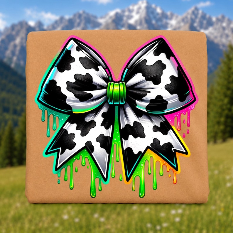 May include: A tan square fabric item featuring a large graphic of a bow with a black and white cow print pattern. The bow has a bright green center knot and is surrounded by vibrant neon-colored paint drips in shades of green, yellow, and pink.