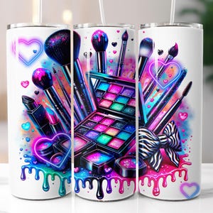 May include: White tumbler featuring a vibrant makeup design. The design includes makeup brushes, an eyeshadow palette, lipstick, and hearts in neon pink, blue, and purple. A zebra-striped bow adds a touch of flair.