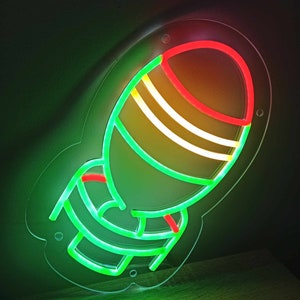 May include: A neon sign shaped like a rocket with a green outline and red and yellow stripes. The sign is lit up and is on a wooden surface.