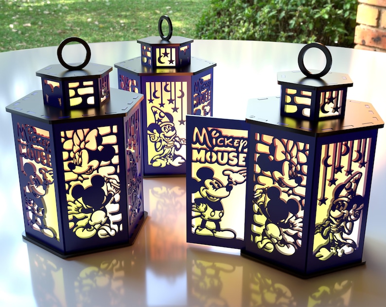 May include: Four dark blue, hexagonal lanterns with black tops and handles. The lanterns feature cut-out designs of Mickey Mouse and friends, with the words "Mickey Mouse" visible on one. The lanterns are illuminated from within.