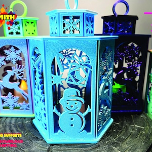 May include: Four 3D printed tealight candle holders in different colors. The holders are hexagonal and feature a snowflake design on the top and a winter scene on the front. The text "CustSmith .STL" is visible on the front of one of the holders.