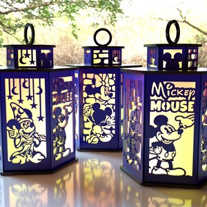 May include: Three navy blue Disney-themed lanterns with cut-out designs featuring Mickey Mouse, Minnie Mouse, and other characters. Each lantern has a black handle and a yellow glow from within, creating a whimsical effect.