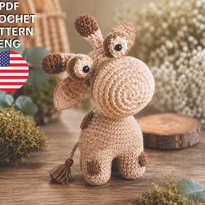 May include: A PDF crochet pattern for a giraffe toy, featuring text that reads PDF CROCHET PATTERN ENG. The giraffe is made of light brown yarn with dark brown spots, a large rounded snout, two small horns, and a tail with a small tassel at the end.