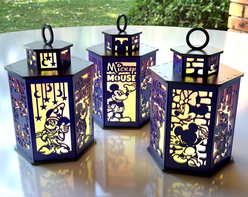 May include: Three illuminated, hexagonal lanterns with black tops and bases. The lanterns feature cut-out designs of Mickey Mouse, Minnie Mouse, and other Disney characters. The sides are a dark blue with yellow-toned light shining through the cutouts.