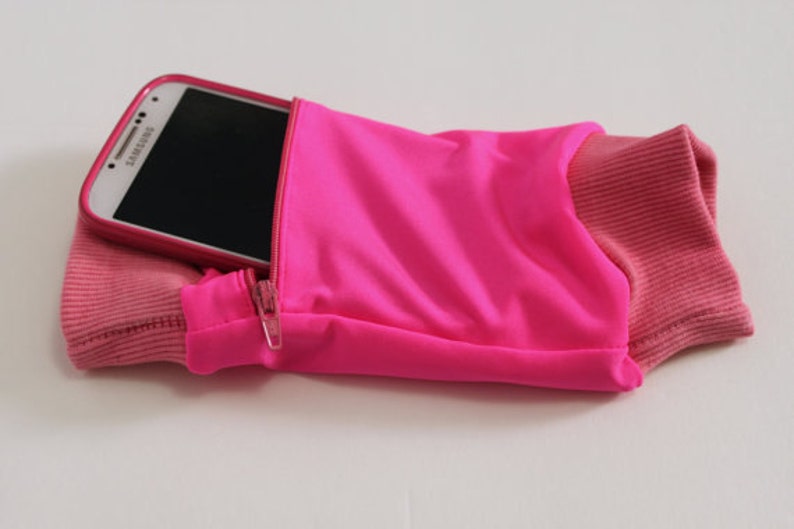 May include: A pink running armband with a zipped pocket to hold a phone. The phone is a Samsung Galaxy.