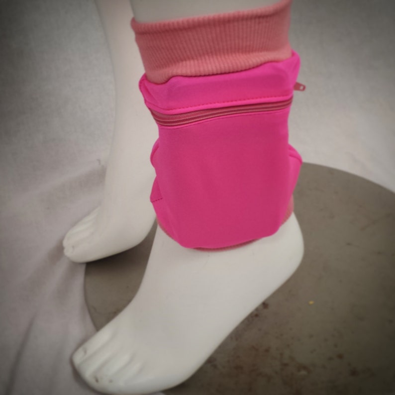 May include: Pink running armband with a zipped pocket. The armband is made of a stretchy material and is designed to fit comfortably on the arm.