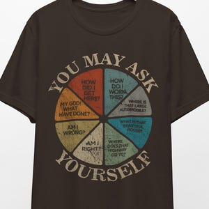 May include: A dark brown t-shirt featuring a pie chart design with questions such as "How did I get here?" and "Where is that large automobile?" The text "YOU MAY ASK YOURSELF" is arched around the chart.