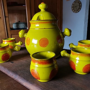 Può includere: Un set di ciotole per zuppa in ceramica gialla con pois arancioni e una ciotola da portata con coperchio abbinata. Le ciotole hanno manici e sono disposte su una superficie in legno.