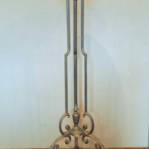 Puede incluir: Un soporte de planta de metal antiguo con una base ornamentada y una parte superior decorativa festoneada. El soporte tiene tres soportes verticales y está acabado en color bronce. El soporte mide aproximadamente 152 cm de altura.
