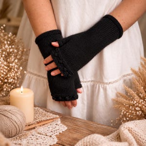 May include: A pair of black fingerless gloves featuring a knitted texture and a decorative row of small, raised bobble details along the cuffs. The gloves extend past the wrists, providing coverage for the forearms while leaving the fingers exposed.