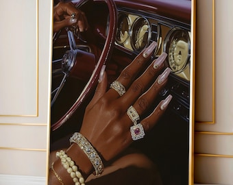 May include: A framed print featuring a close-up of a person's hand adorned with multiple rings and a bracelet, resting on a car's steering wheel. The hand has long, light pink nails. The car's interior is a deep red.