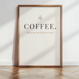 Puede incluir: Un cartel enmarcado con marco de madera. El cartel tiene la palabra "COFFEE" en negrita, en color marrón oscuro, con líneas de vapor encima de la palabra. Debajo está la frase: "Because adulting is hard."