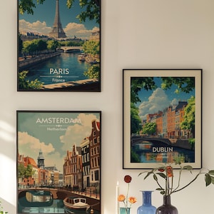 May include: Three framed vintage travel posters with images of Paris, Amsterdam, and Dublin. The posters are hanging on a white wall with a vase of flowers and candles in front of them.