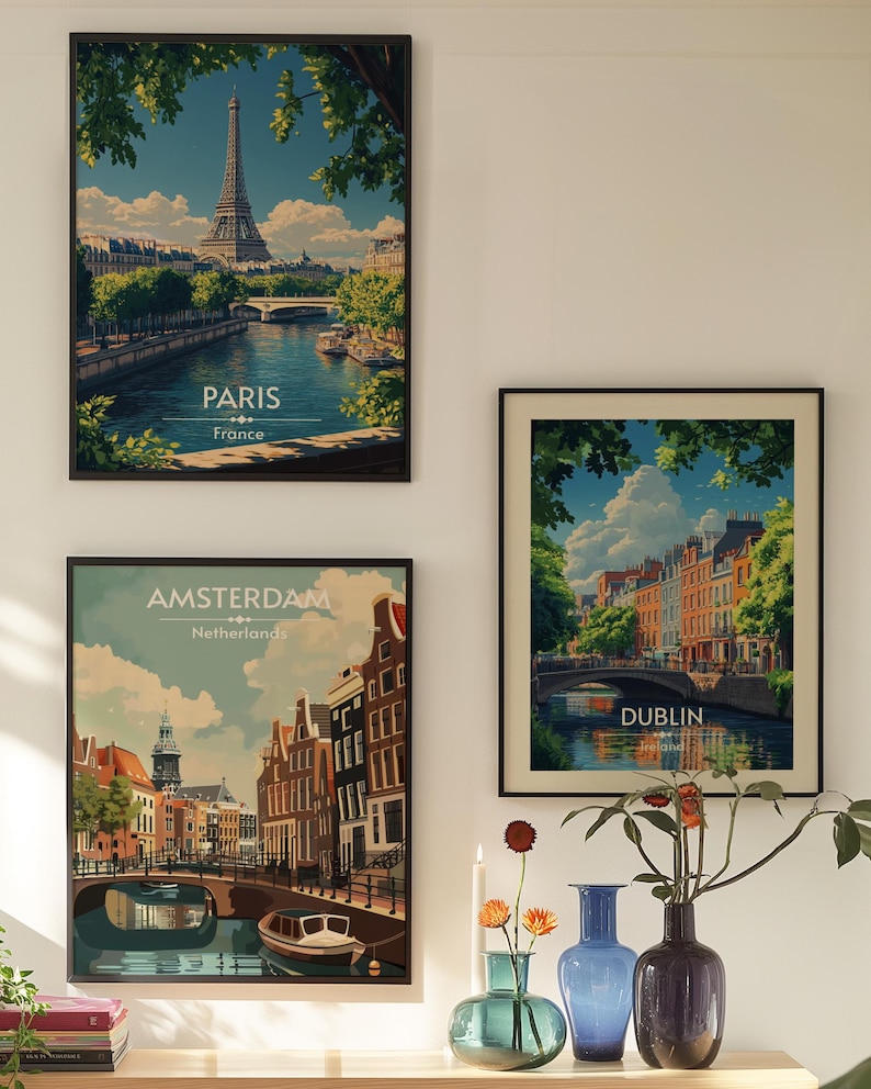May include: Three framed vintage travel posters with images of Paris, Amsterdam, and Dublin. The posters are hanging on a white wall with a vase of flowers and candles in front of them.