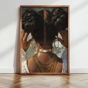 Può includere: Stampa artistica incorniciata raffigurante una persona con capelli scuri acconciati in due chignon. La persona indossa orecchini a cerchio dorati, un girocollo dorato con un accento bianco a forma di diamante e collane a catena dorate multiple. L'immagine è incorniciata in una cornice di legno marrone.