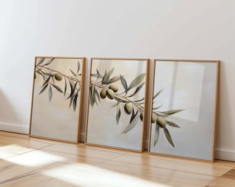 May include: A set of three framed prints featuring a watercolor painting of olive branches with green olives. The prints are in a light wood frame and are displayed on a light wood floor.